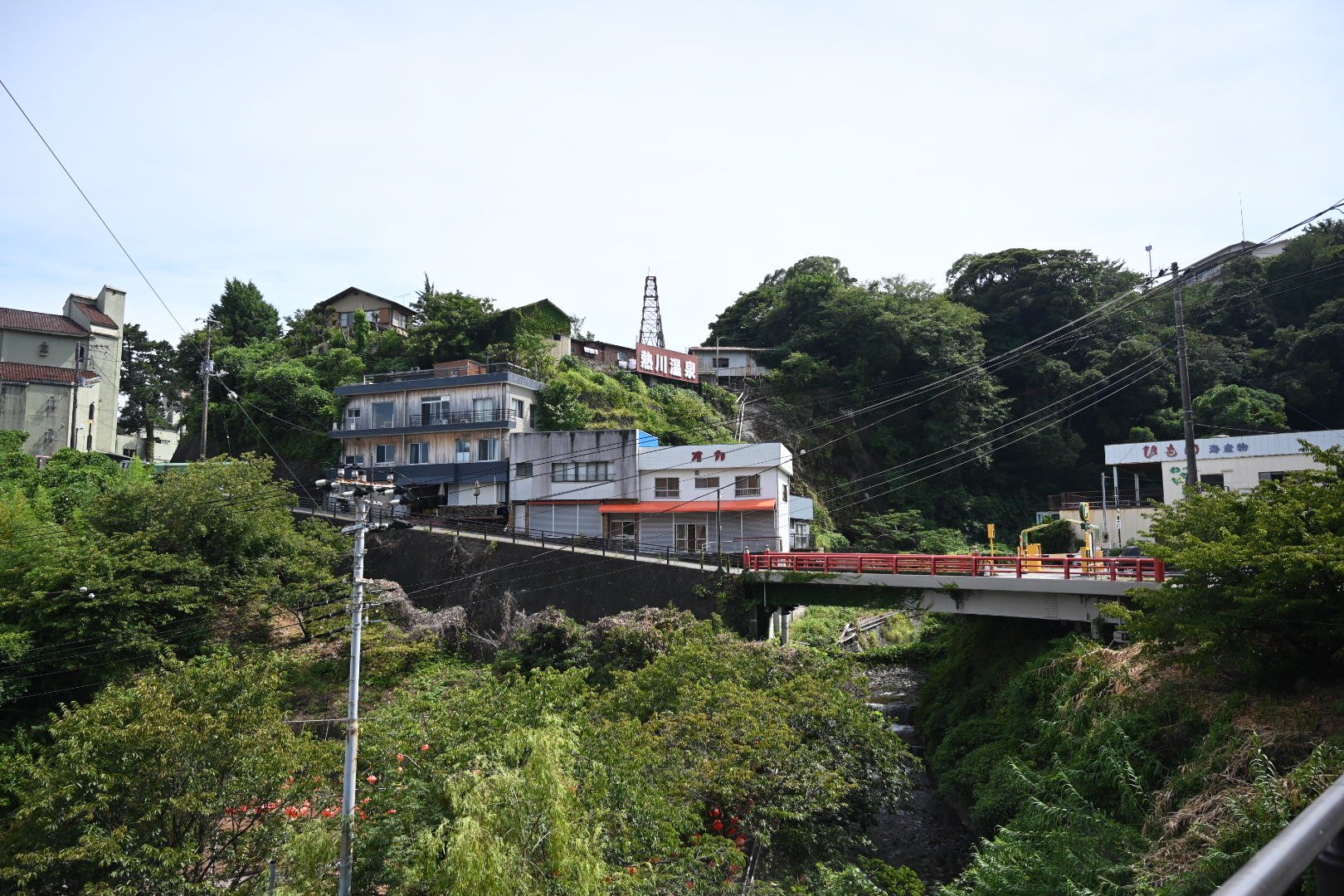 熱川温泉の赤い橋と、崖の上に立つ「熱川温泉」の看板と温泉やぐら