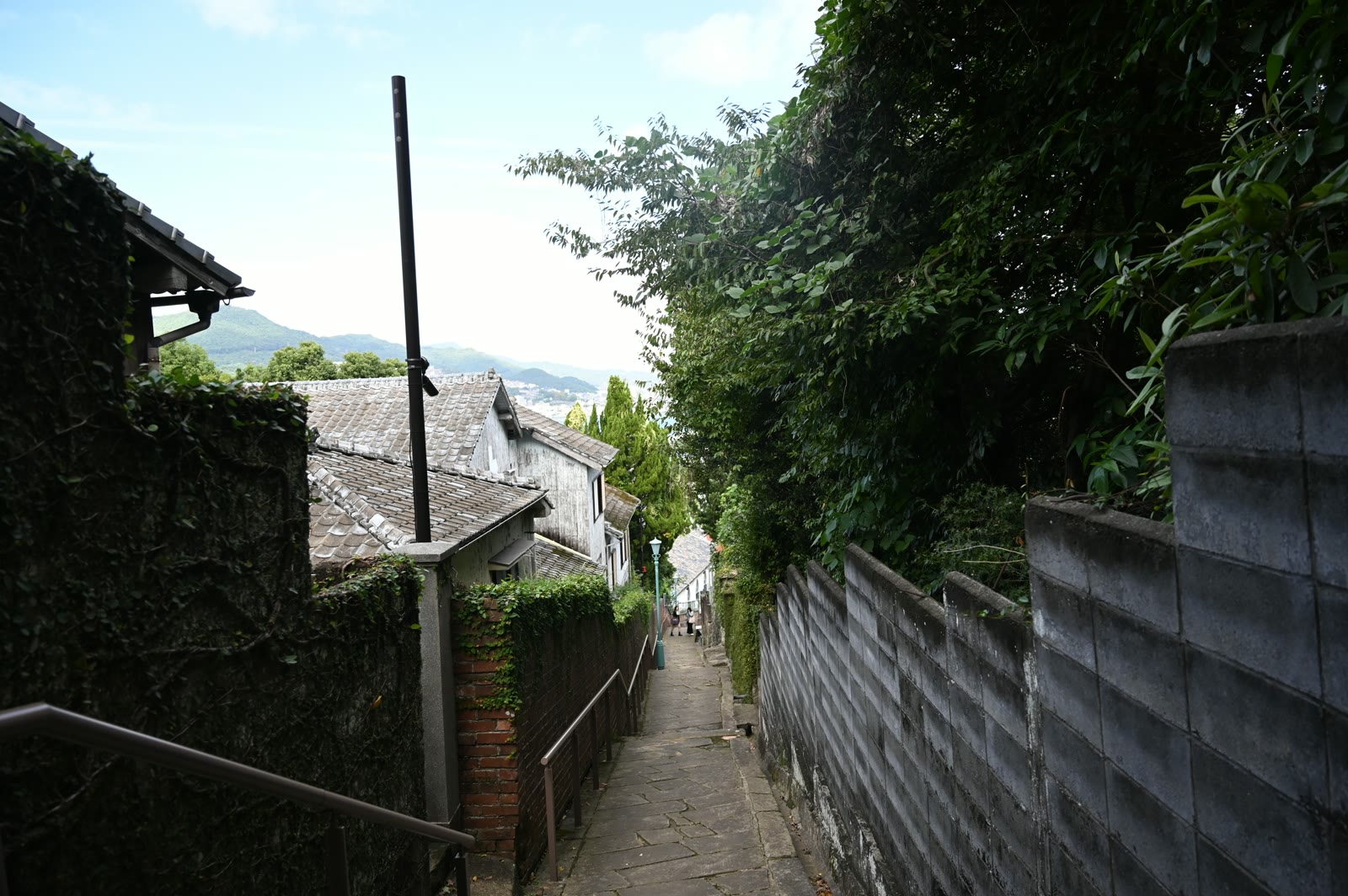 長崎・南山手の祈念坂。古い家の壁と緑のあいだを下る細い石畳の坂