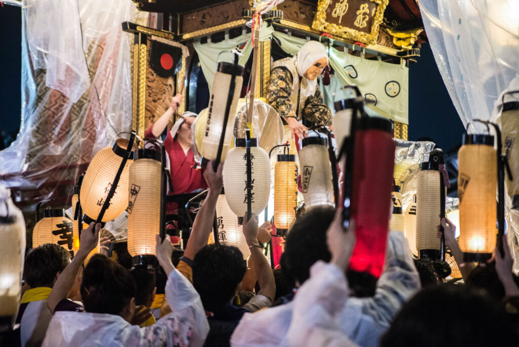 山車の前で祭り人たちが提灯を高く掲げる曳っかわせ