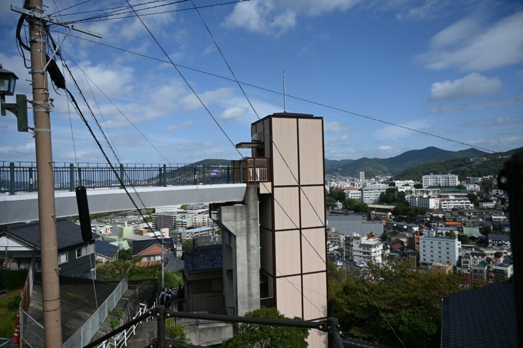 グラバースカイロードのエレベーターの塔と連絡橋、長崎港の眺め