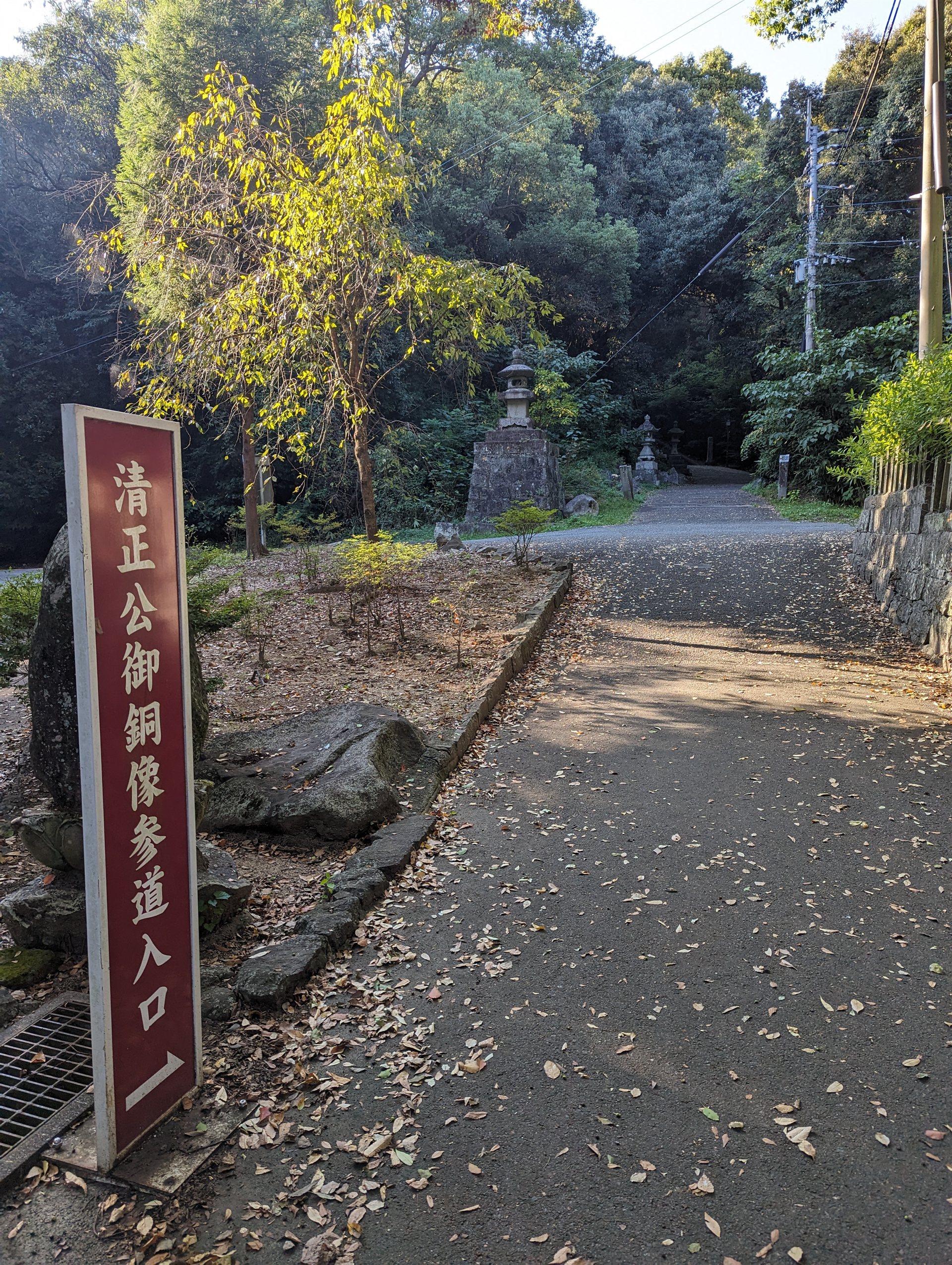 本妙寺の「清正公御銅像参道入口」と書かれた赤い案内札と、木陰の道