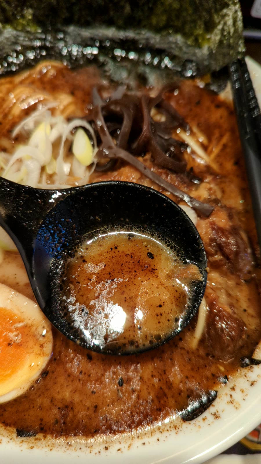 おっぺしゃん熊本本店のラーメンのスープ。黒マー油が浮かぶ豚骨スープをれんげですくったところ