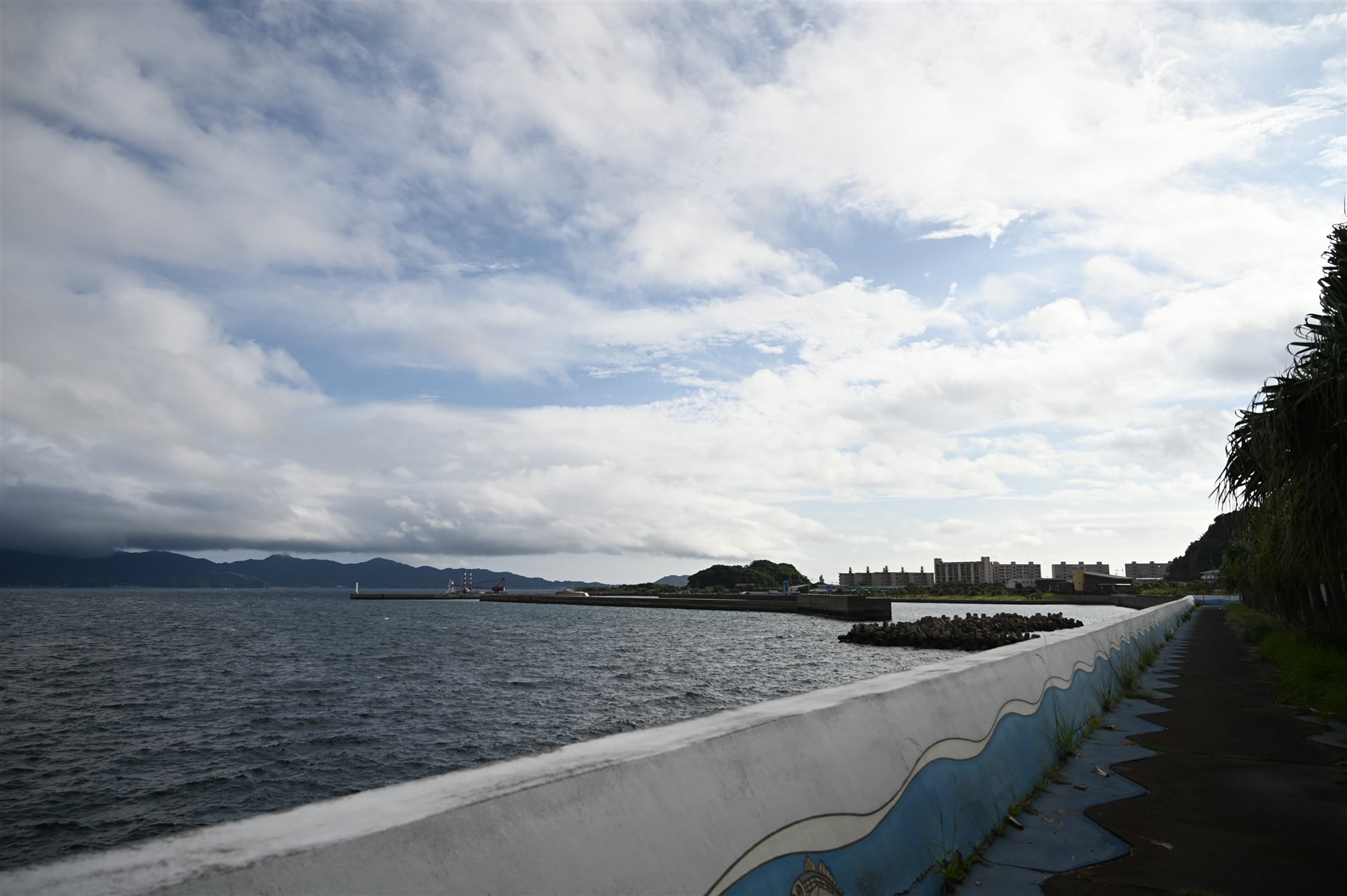 長崎・高島の波の絵が描かれた堤防と海沿いの道。遠くに港と建物