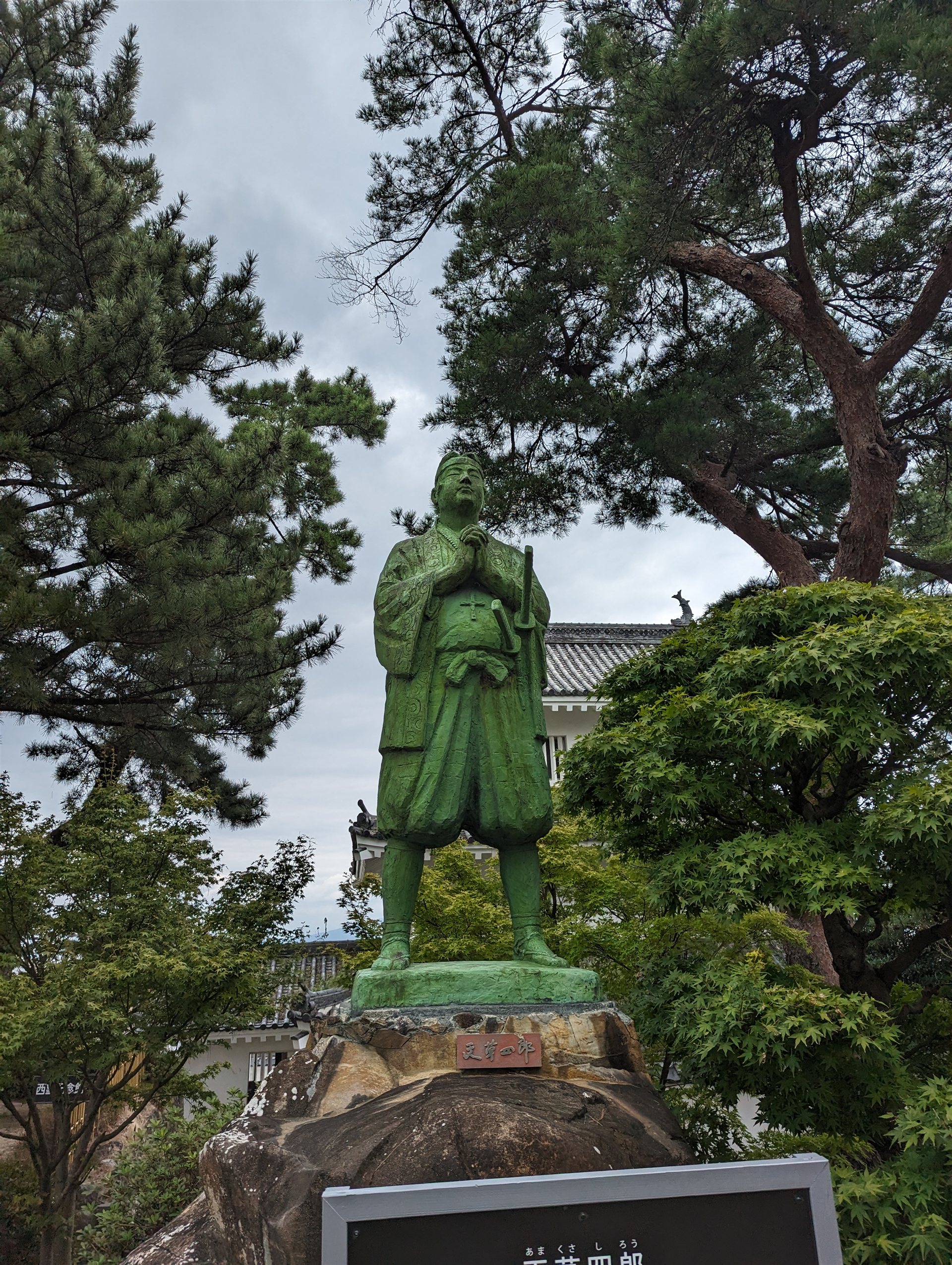 島原城の本丸で手を合わせて立つ天草四郎の像と、うしろの松の木